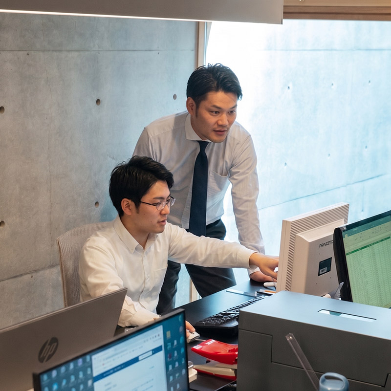 PCの画面を一緒に見ながら、業務について真剣に相談し合う二人の男性社員。