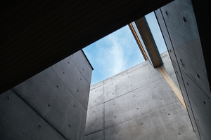 コンクリート打ち放しの建築空間に設けられた吹き抜けから空を望む様子